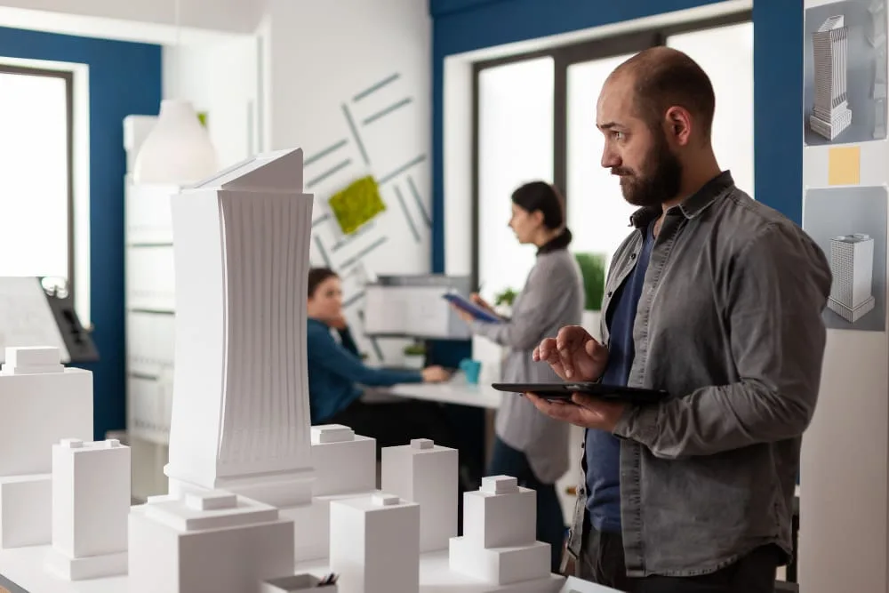 Architect holding a tablet beside white architectural scale models
