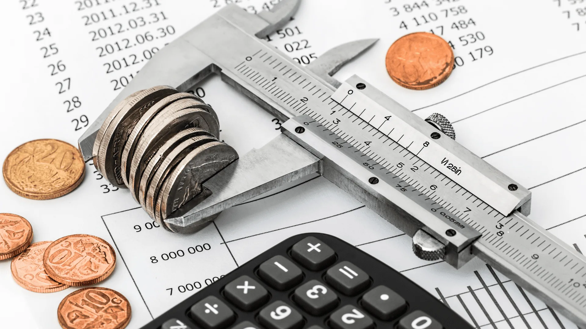 Caliper measuring a stack of coins beside a calculator on a budget sheet