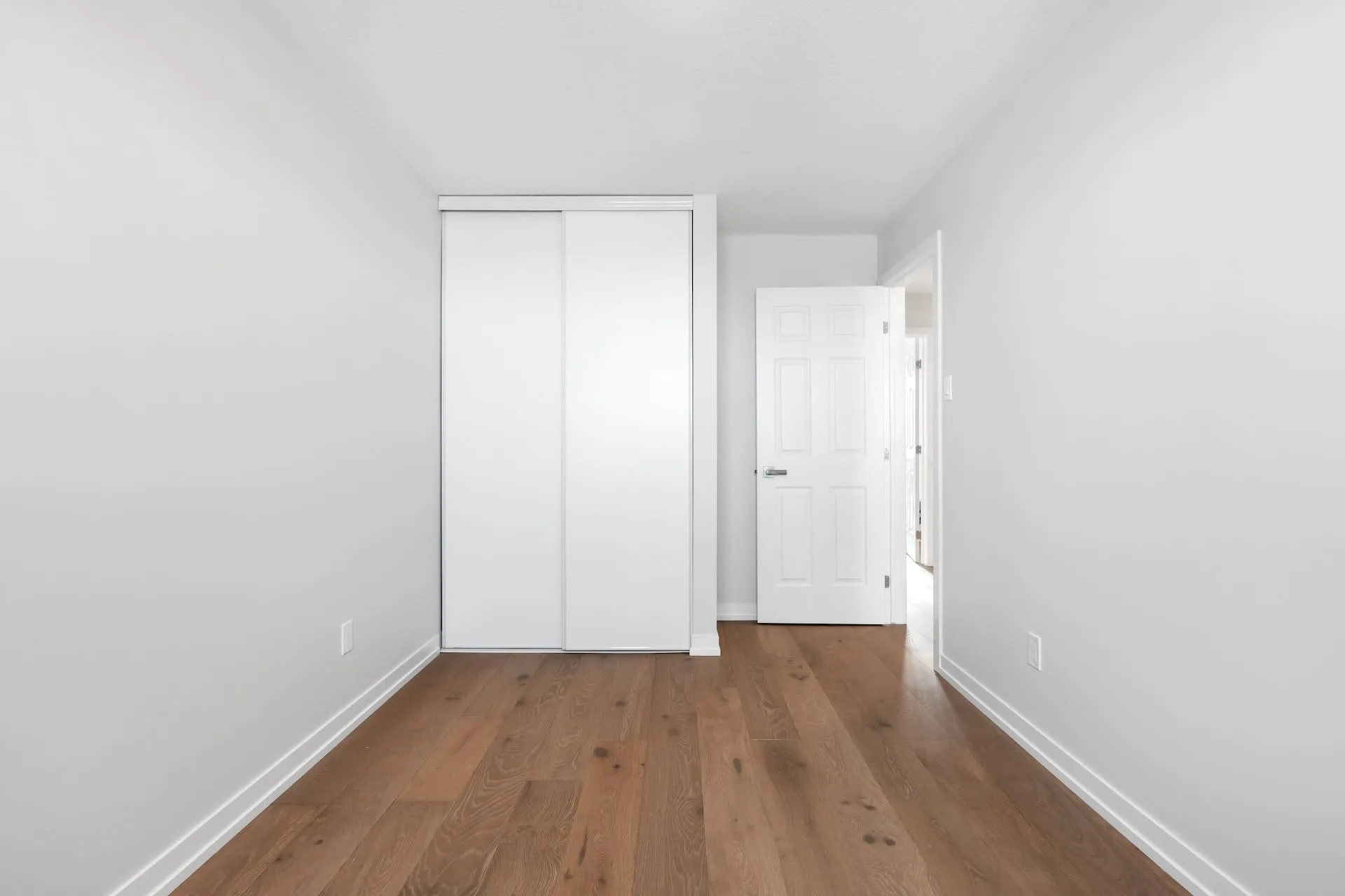 Empty bedroom with new wood plank flooring and white closet doors