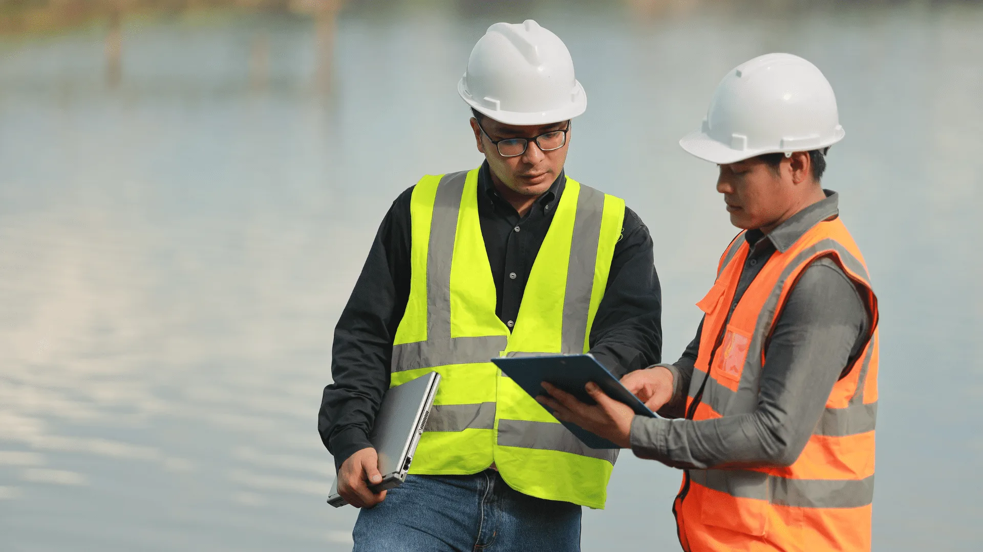 Two engineers in hard hats reviewing a site plan on a tablet