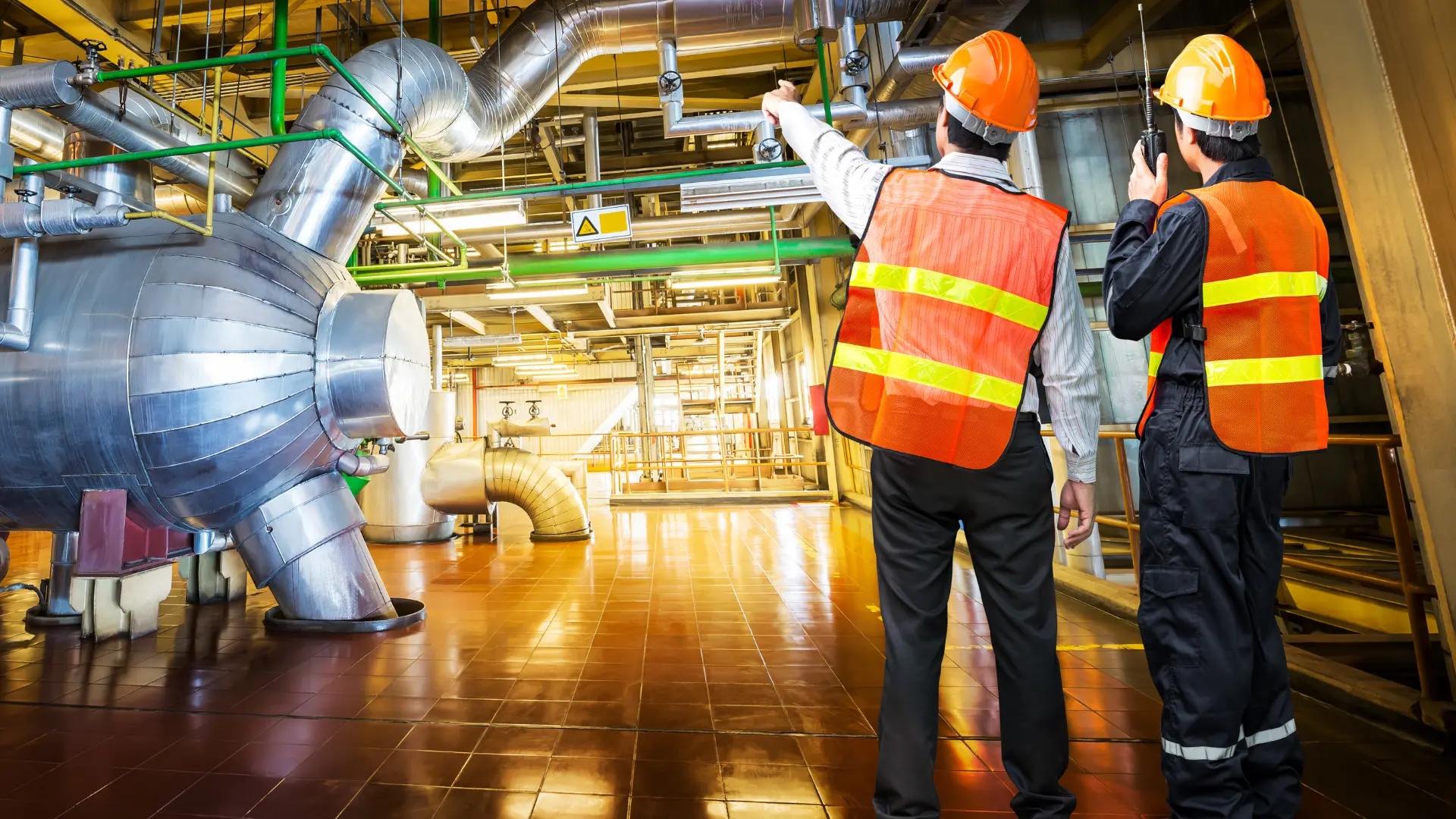 Two engineers in hard hats inspecting ductwork in a mechanical room