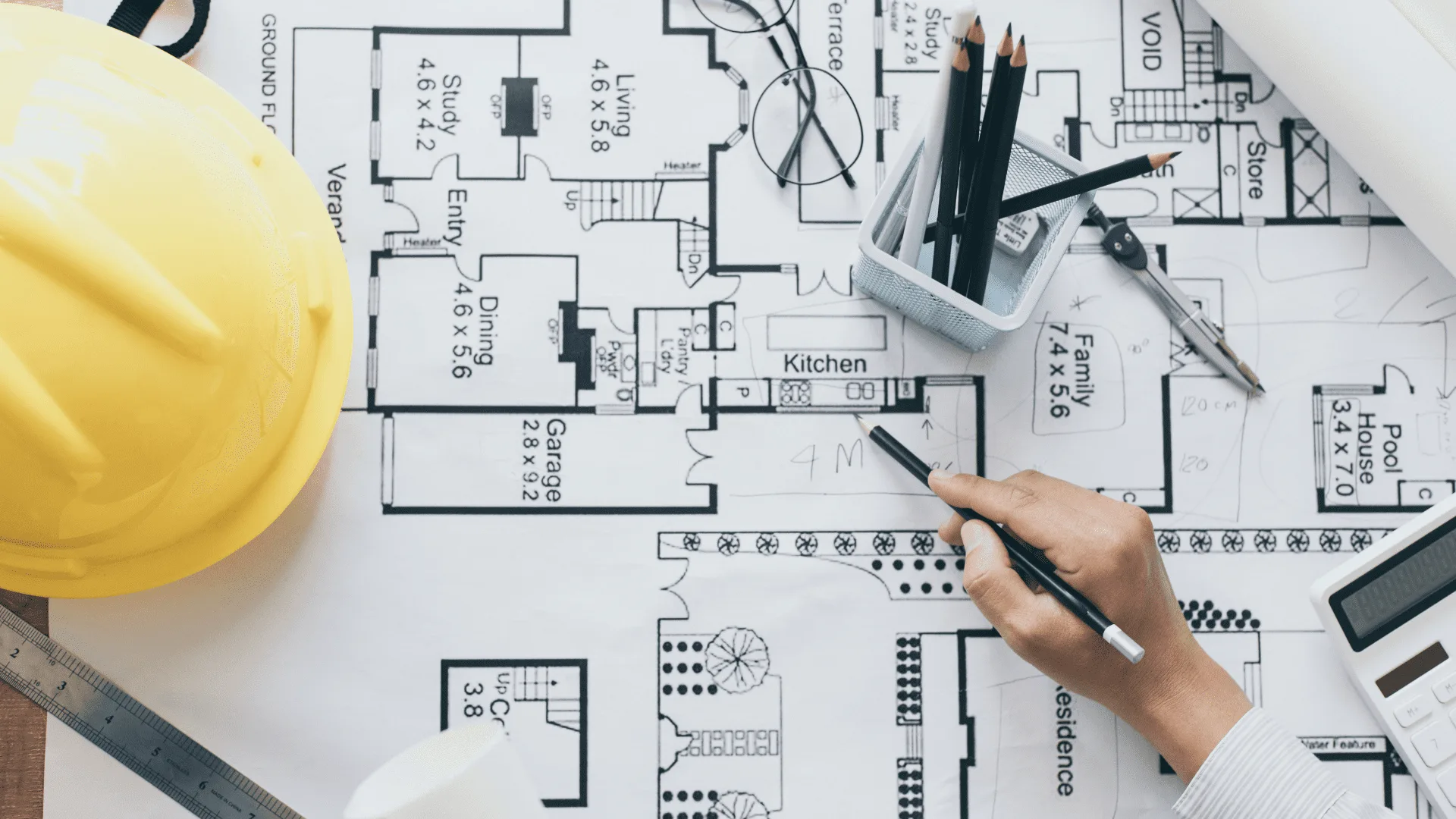 Hand marking up residential floor plans next to a yellow hard hat