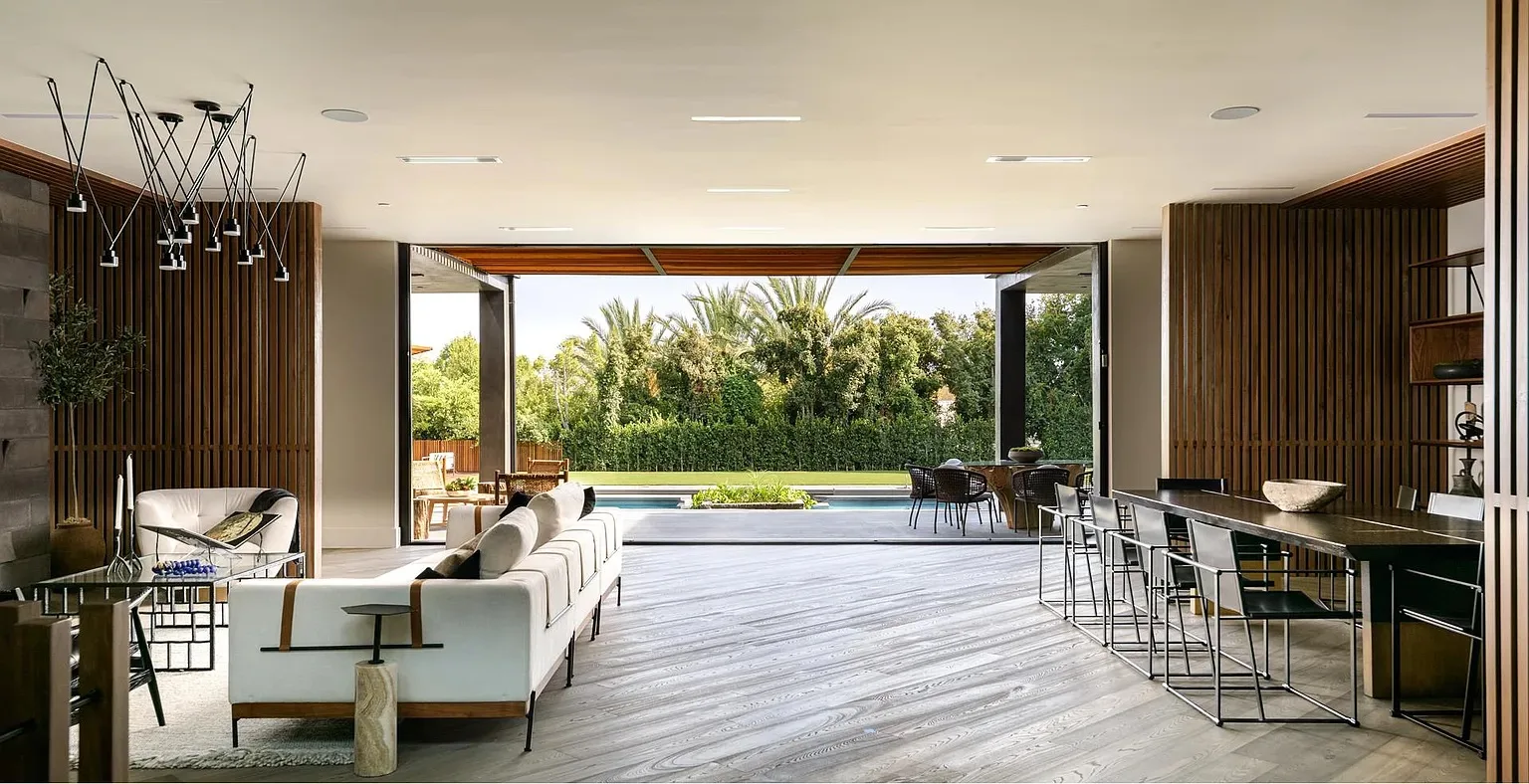 Indoor outdoor living room opening through retracted glass walls to the pool terrace