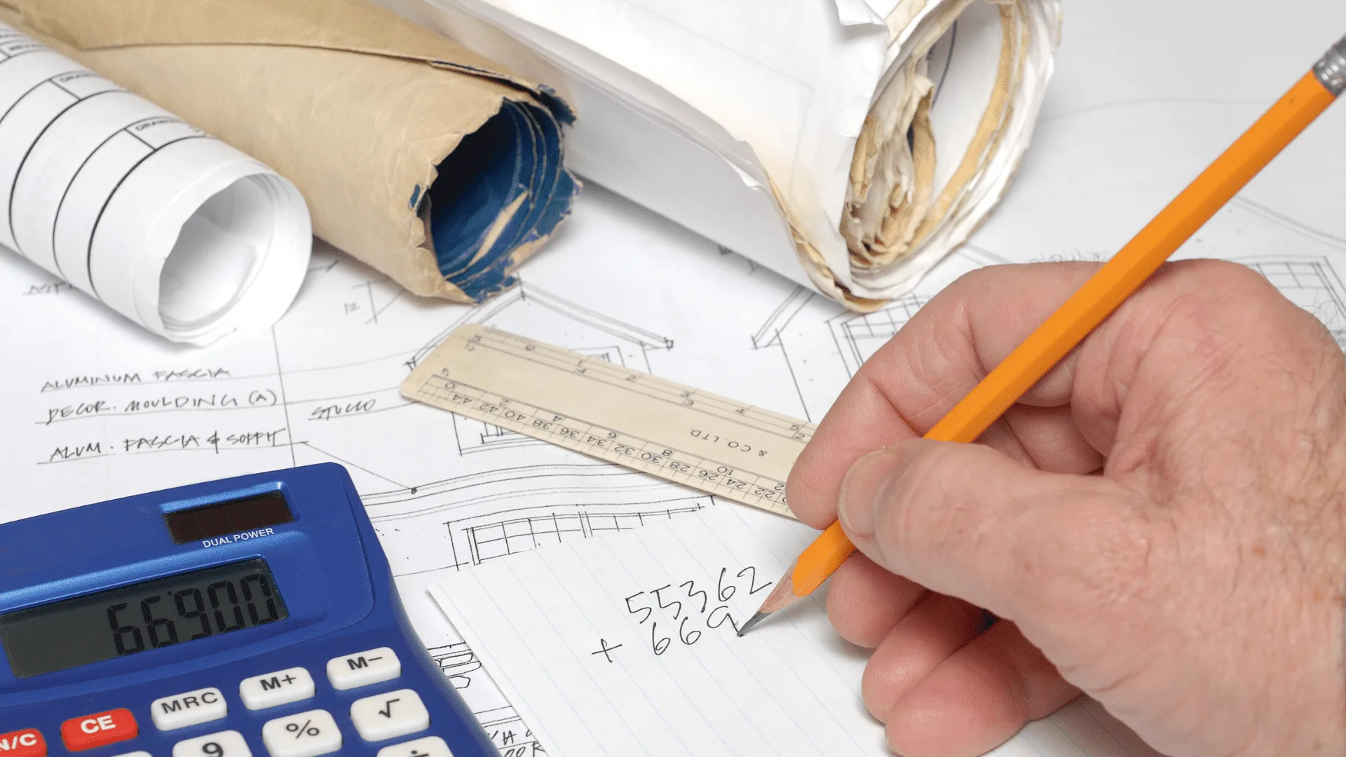 Estimator calculating quantities with a pencil, ruler and calculator over drawings