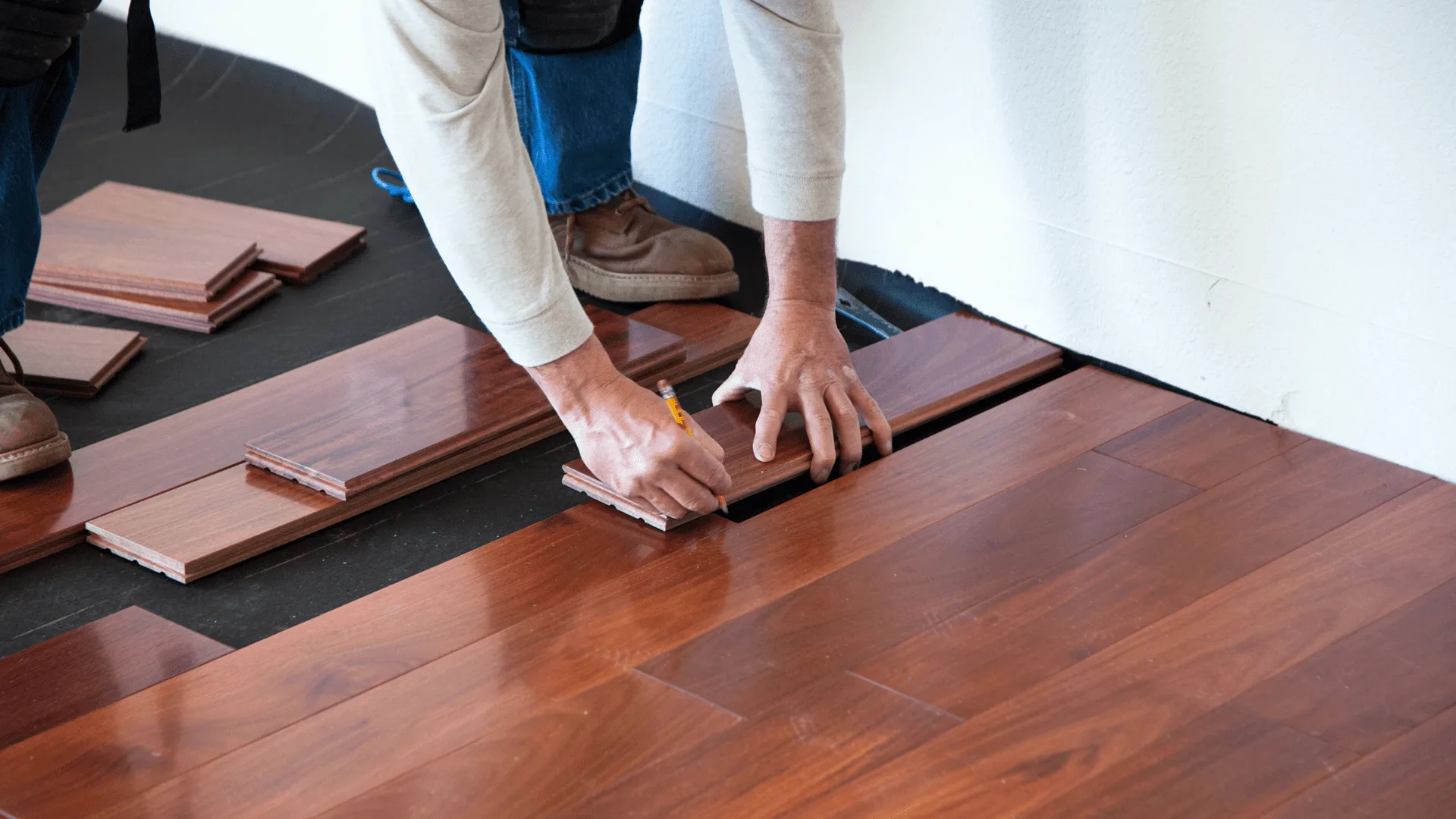 Installer fitting hardwood floor planks over underlayment