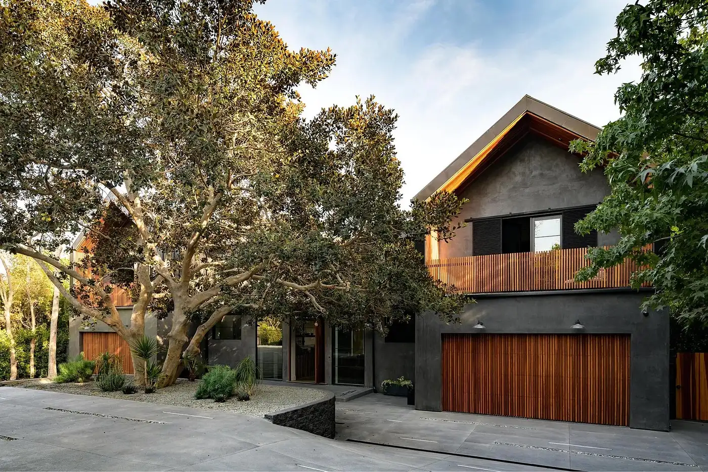 Modern exterior renovation with charcoal stucco and wood cladding under a mature oak