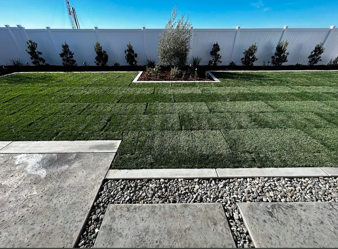 Backyard with new sod lawn, concrete pavers and gravel joints along a white fence