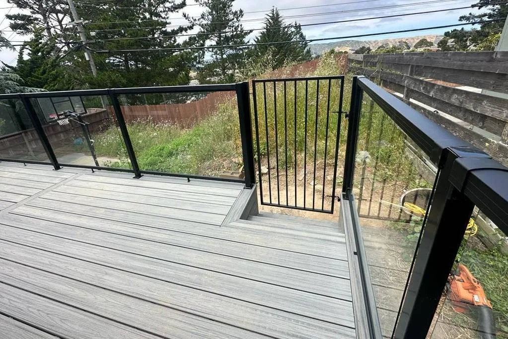 Grey composite deck with black-framed glass railing panels and a metal gate at 477 Nevada St, San Francisco