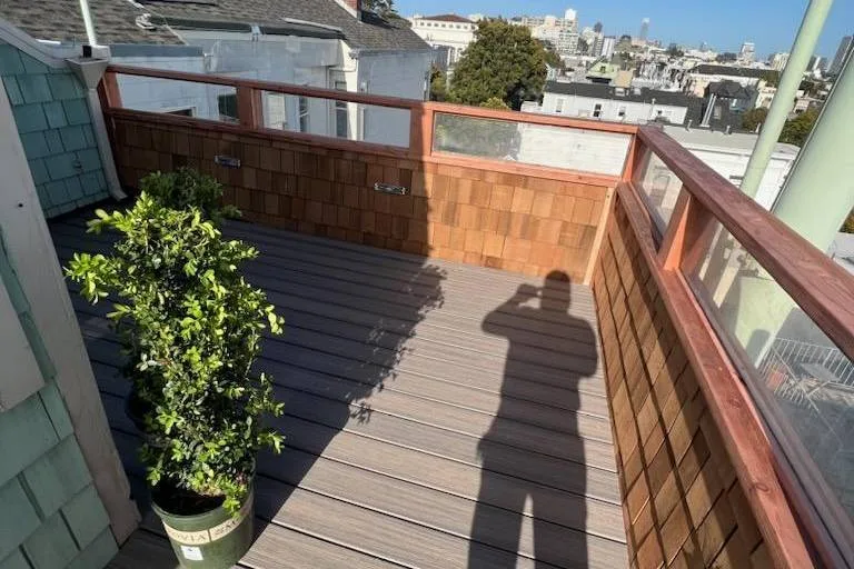 Upper-level deck with brown composite boards, cedar shingle walls and glass panels on Brodrick Street, San Francisco