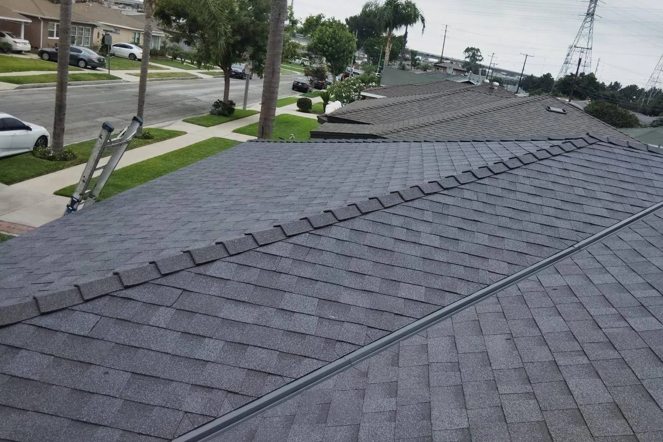 New dark grey asphalt shingle roof with ridge caps above a residential street on Howery St, South Gate