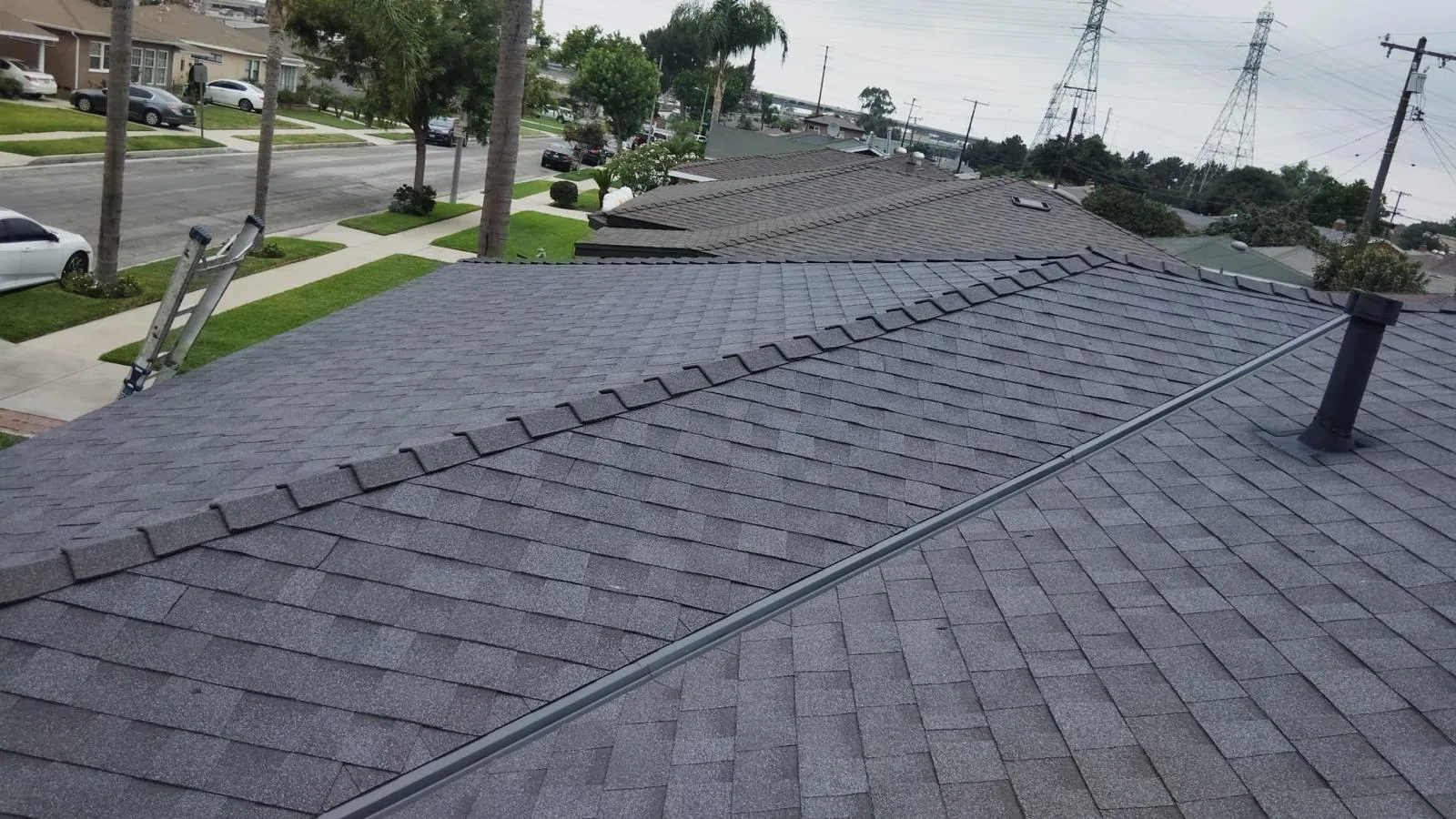 Wide view of the finished dark grey shingle roof and vent pipe over the street on Howery St, South Gate