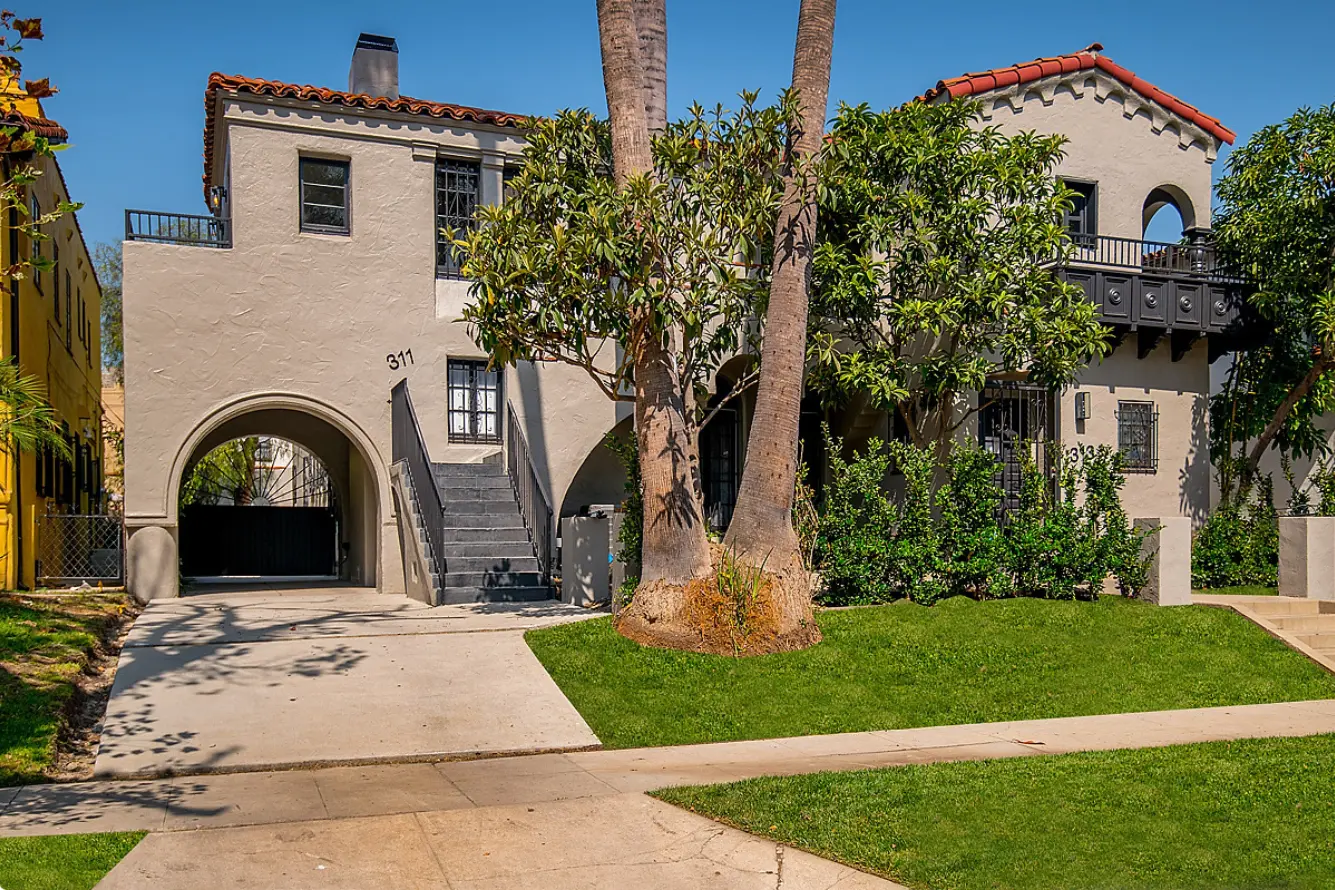 Spanish-style two-storey stucco home with a red clay tile roof, an arched drive-through entry and a front lawn on N Mansfield, Los Angeles