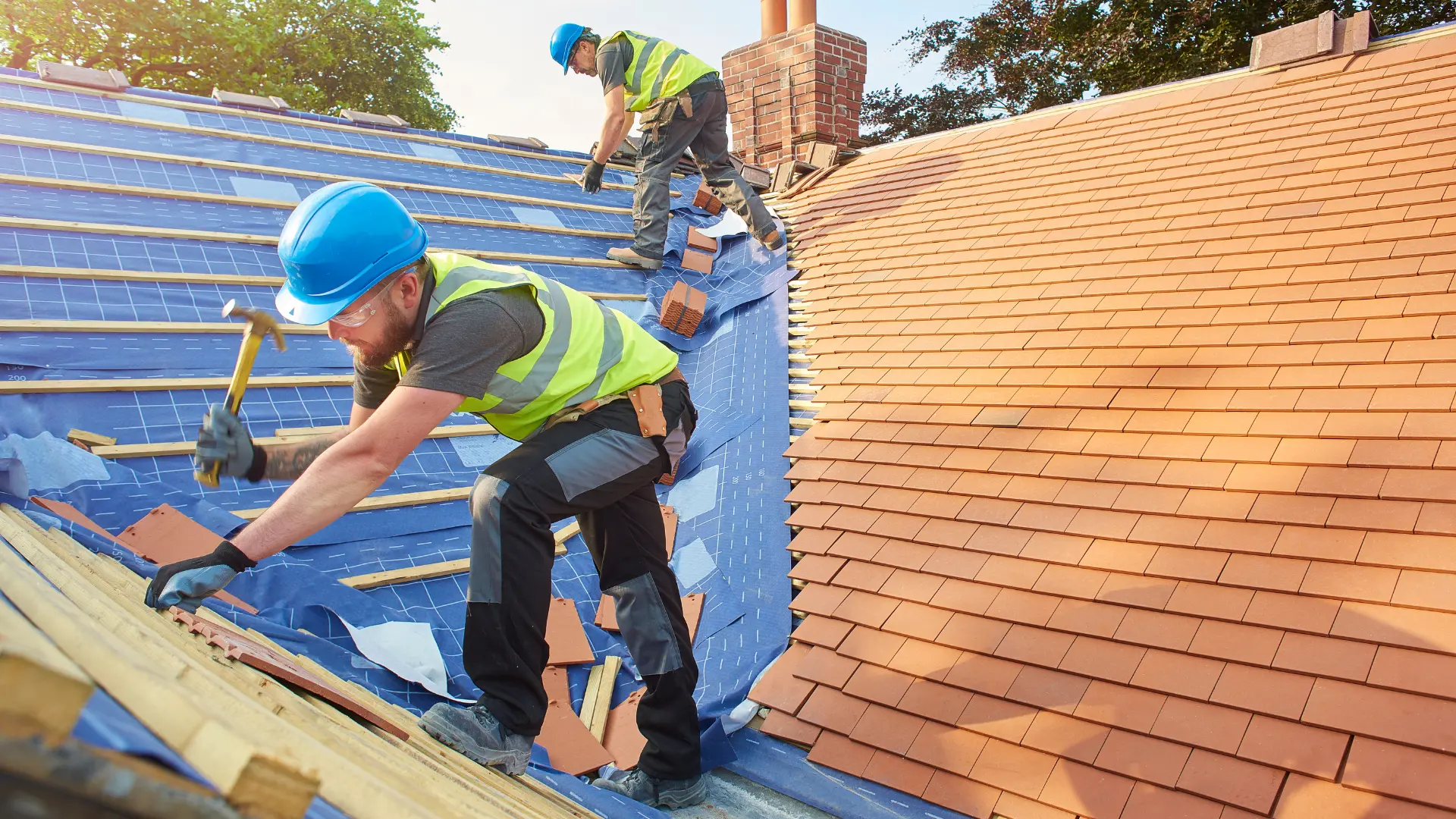 Roofer in a hard hat installing clay roof tiles over underlayment