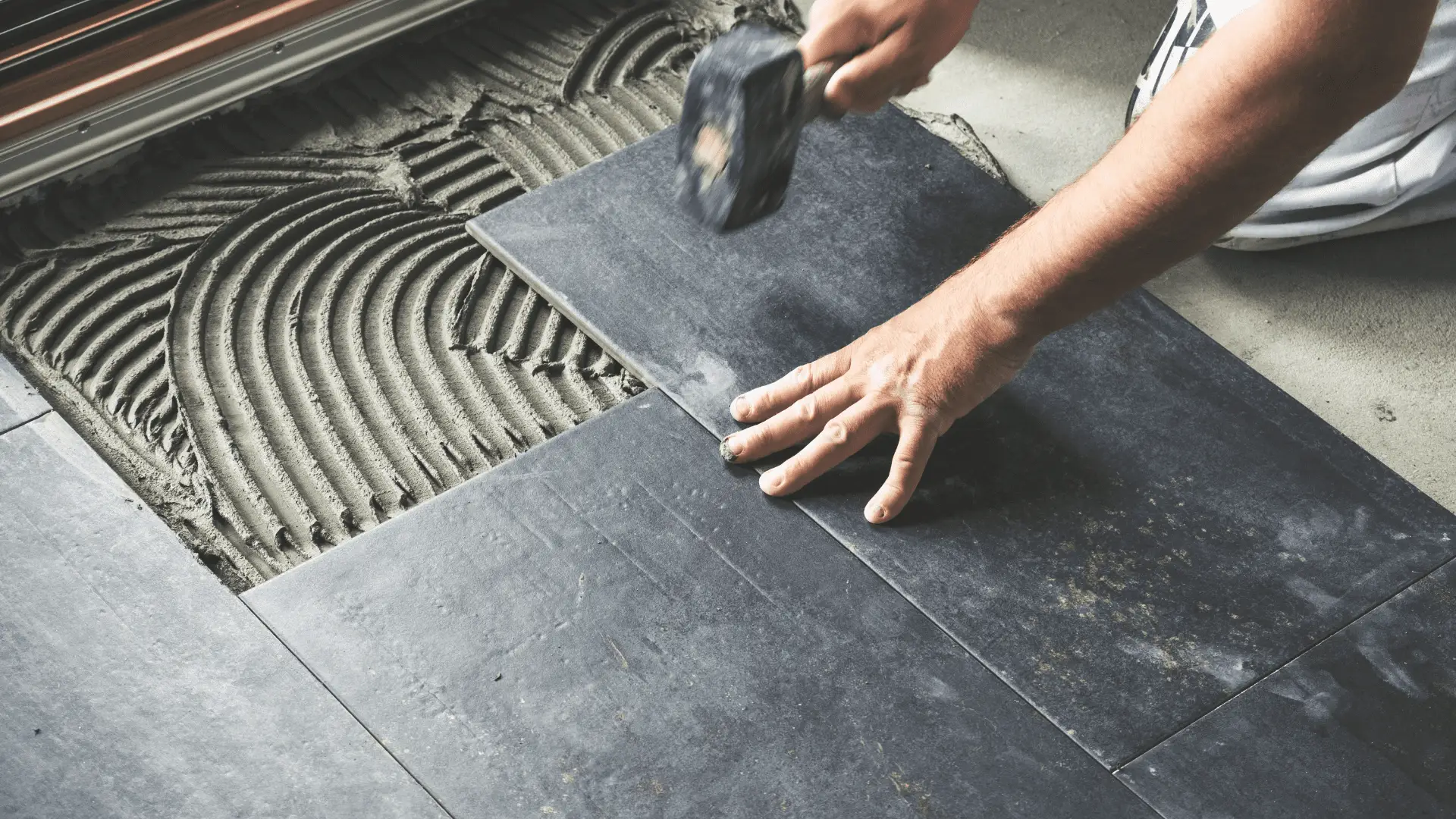 Installer setting a dark floor tile into thinset with a rubber mallet