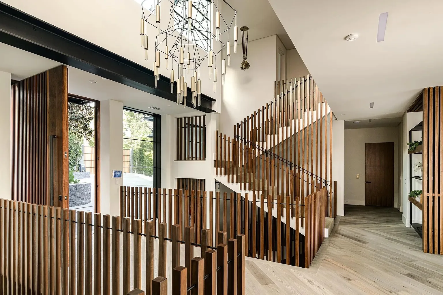 Architectural wood slat staircase under a double-height ceiling with a sculptural chandelier