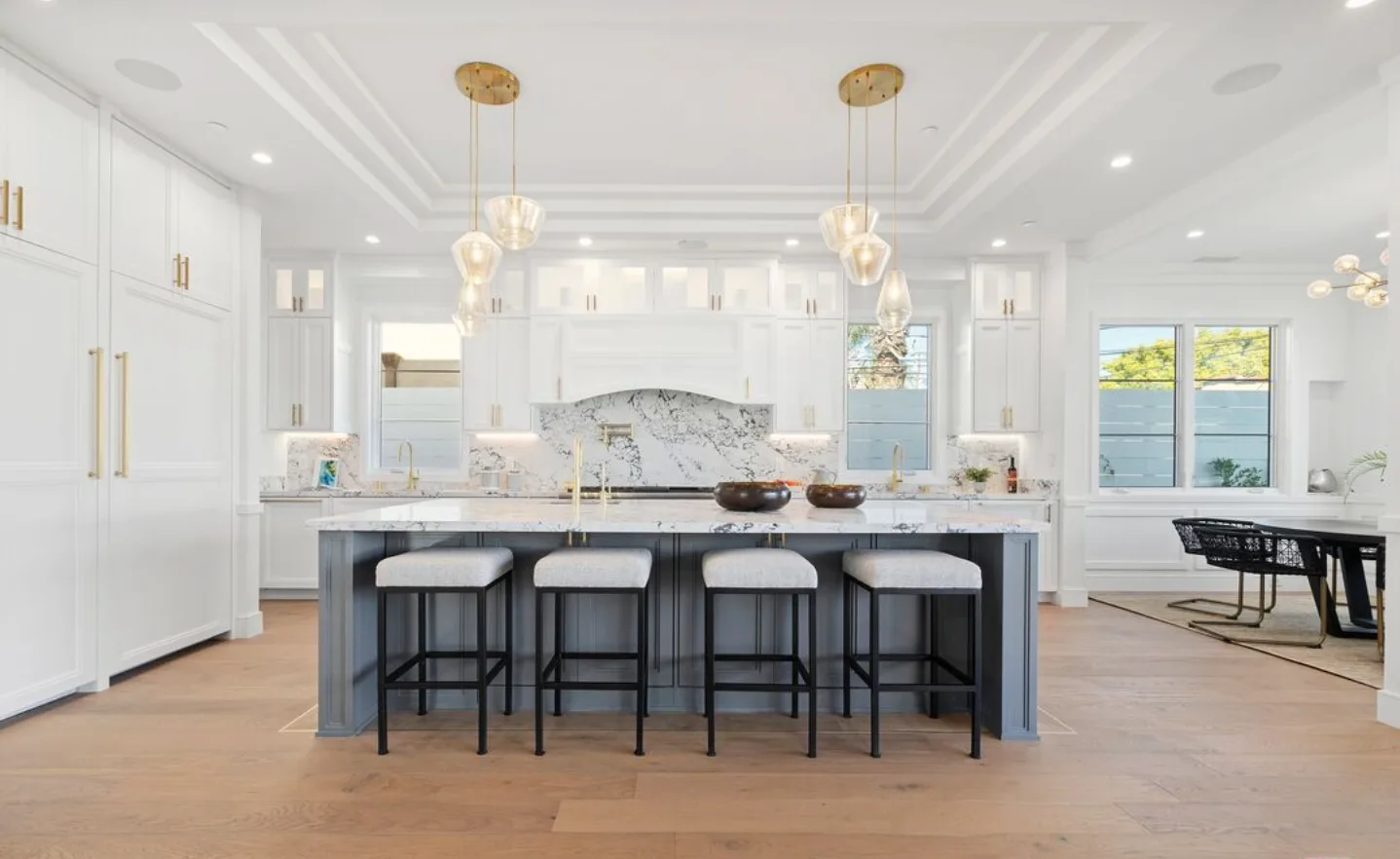 Completed kitchen with a blue-gray island, counter stools and brass pendant lights